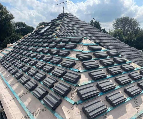 This is a photo of a new hip roof being installed. New felt, battens, and grey tiles have been installed, also a new velux window. Works carried out by SM Roofing Hatfield