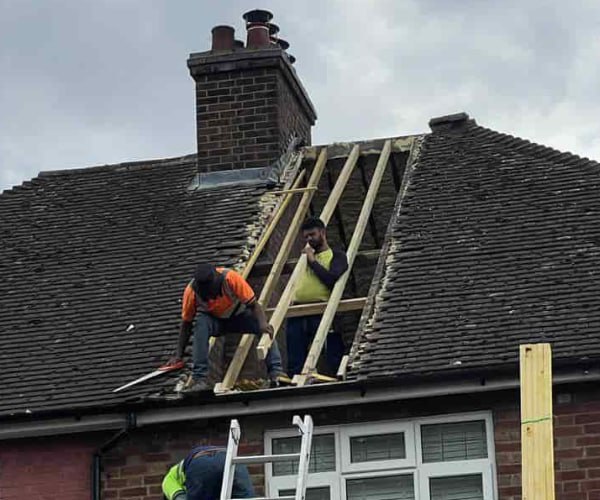 This is a photo of a roof repair being carried out. A section of the roof has been stripped and two roofers are replacing the rafters. Works being carried out by SM Roofing Hatfield